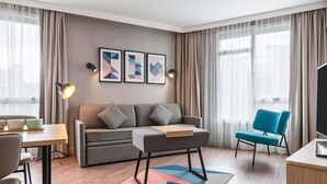 A modern hotel room with a sofa, a blue armchair, a TV, a desk, and a coffee table. - Aparthotel Adagio Paris Nation (Paris)