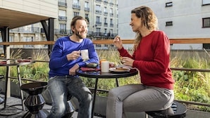 Two people seated at an outdoor table with a cityscape view, a metal chair, and a small table with a cup and a plate. - Aparthotel Adagio Paris Nation (Paris)