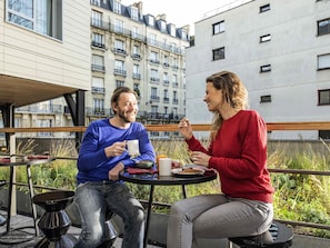 Two people seated at an outdoor table with a cityscape view, a metal chair, and a small table with a cup and a plate. - Aparthotel Adagio Paris Nation (Paris)