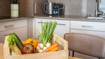 Una cocina con un cesto de madera lleno de verduras frescas, una cafetera y un grifo moderno.