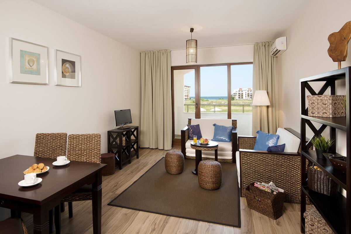 Un salon moderne comprenant un coin repas, un téléviseur, des meubles en osier et une vue sur la mer.