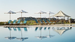 Een zwembadterras met ligbedden en parasols, met weerspiegeling van het zwembad en de omliggende gebouwen.