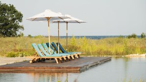 Een houten terras met lounge stoelen en parasols, uitkijkend op een rustig wateroppervlak.