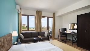Een hotelkamer met een bed, een bank, een bureau met een televisie en uitzicht op het strand.