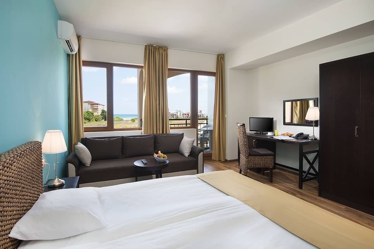 Une chambre d’hôtel avec un lit, un canapé, un bureau avec une télévision et une vue sur la plage.