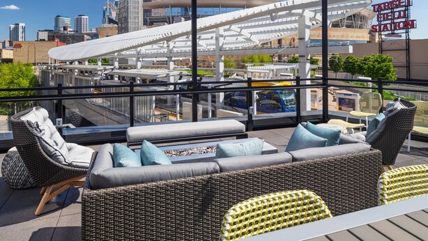 A rooftop terrace with wicker furniture, a view of the city skyline, and a Target Field Station sign. - Element by Marriott Minneapolis Downtown (Minneapolis)