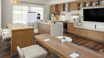 Une cuisine moderne avec des meubles en bois, un grand téléviseur et un coin repas comprenant une longue table et des chaises.