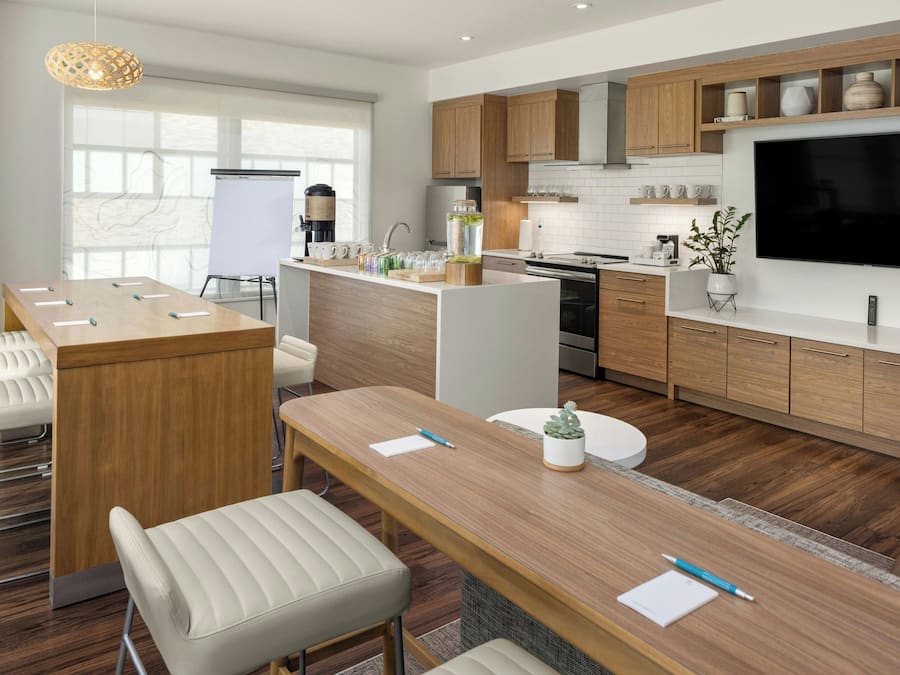 Une cuisine moderne avec des meubles en bois, un grand téléviseur et un coin repas comprenant une longue table et des chaises.