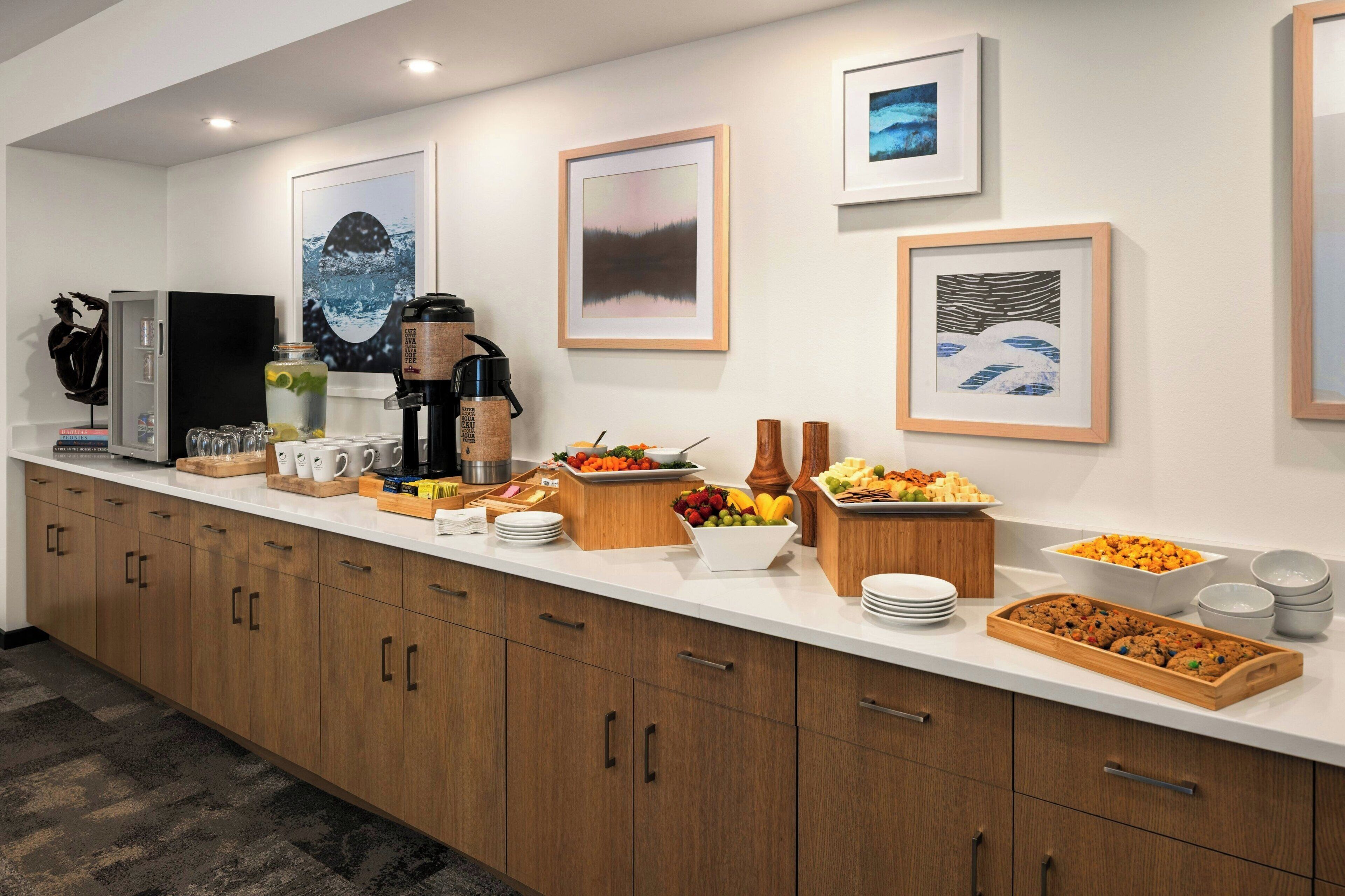 Una cocina moderna con una encimera larga, varios alimentos, una máquina de café y cuadros en la pared.