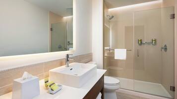 A modern bathroom with a large mirror, a white sink, a toilet, and a glass-enclosed shower.
