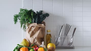 Una encimera de cocina con productos frescos, una bolsa de papel, una botella de aceite y utensilios.