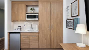 Una cocina moderna con armarios de madera, microondas y lavavajillas. Hay cuadros en la pared y una mesa con una lámpara.