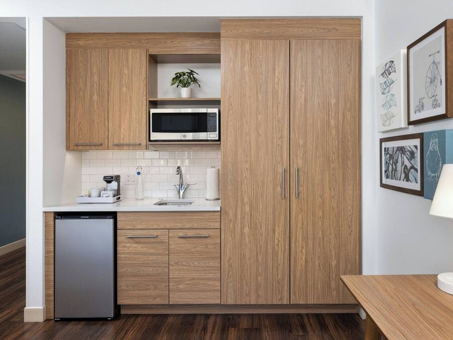 Una cocina moderna con armarios de madera, microondas y lavavajillas. Hay cuadros en la pared y una mesa con una lámpara.
