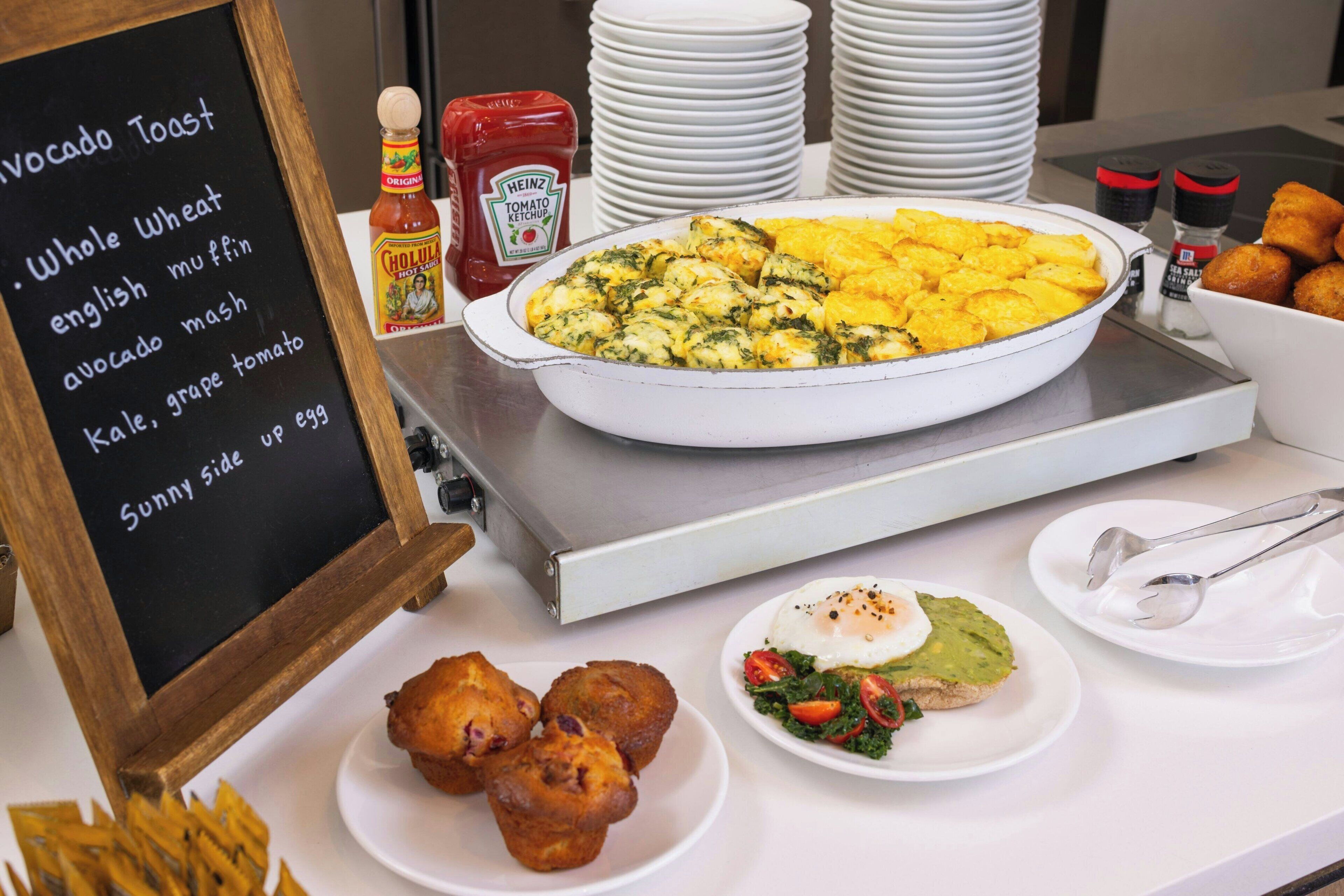 Un bufé de desayuno con diversos platos, incluyendo tostadas de aguacate, muffins y una tortilla grande.