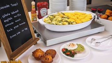 Un bufé de desayuno con diversos platos, incluyendo tostadas de aguacate, muffins y una tortilla grande.