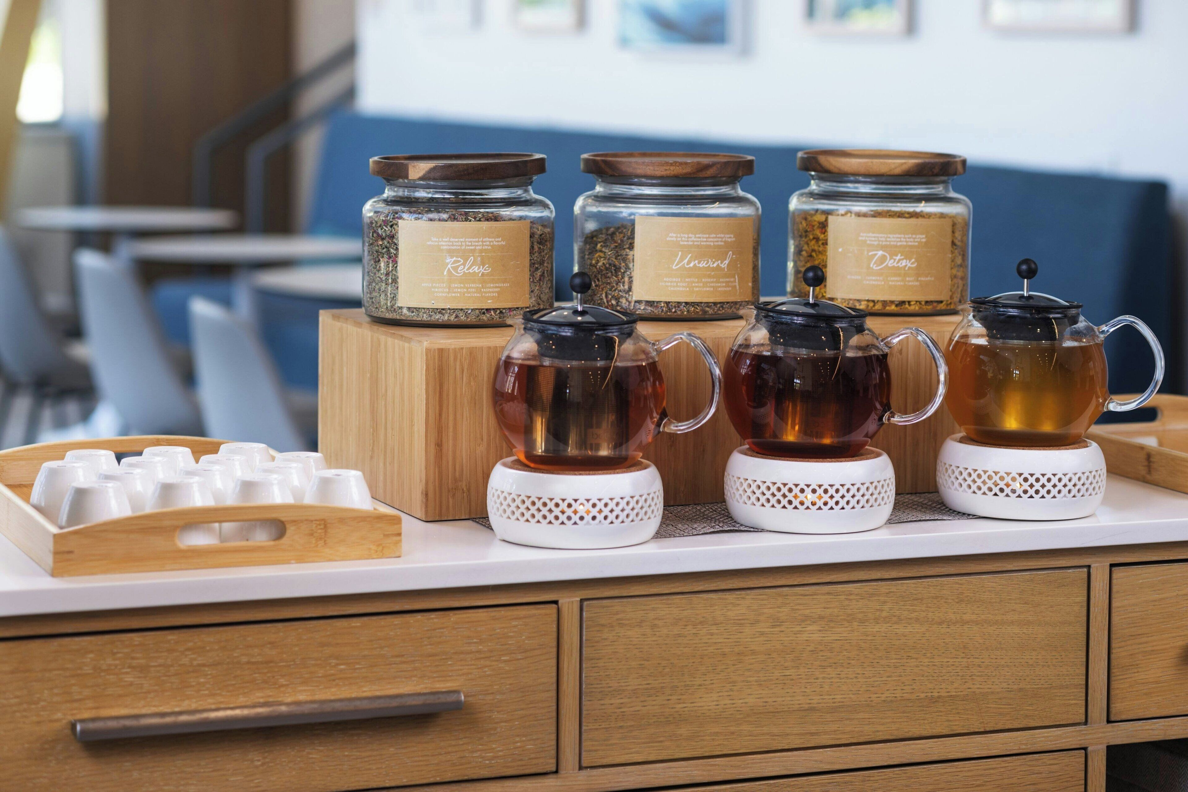 A coffee station with jars labeled 'Kilo', 'Unmond', and 'Detox' on a wooden counter.