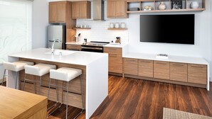 Una cocina moderna con una isla central, taburetes de bar, armarios de madera, horno empotrado y un televisor de pantalla plana grande.