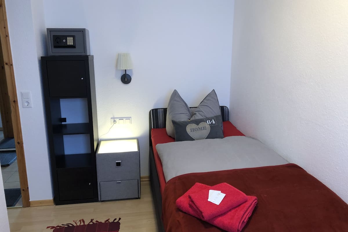 A bedroom with a bed, a nightstand, a desk, and a lamp.