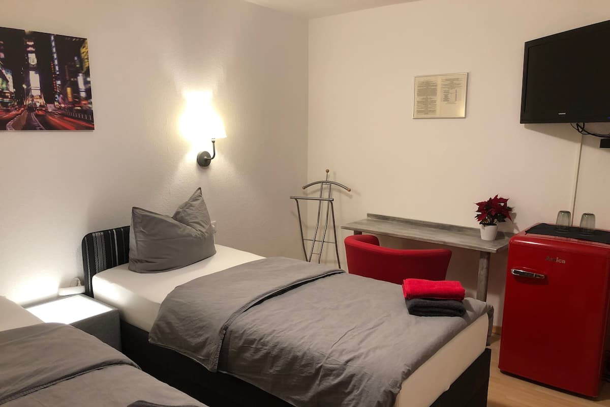 A hotel room with two beds, a desk, a TV, and a small fridge.