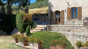 A stone house with a tiled roof, a gated entrance, and a well-maintained garden with potted plants.