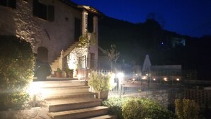 A stone staircase leading to a building with a lighted entrance, surrounded by potted plants and a fence.