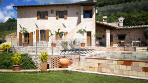 A stone villa with a swimming pool, outdoor seating, and a mountainous backdrop.