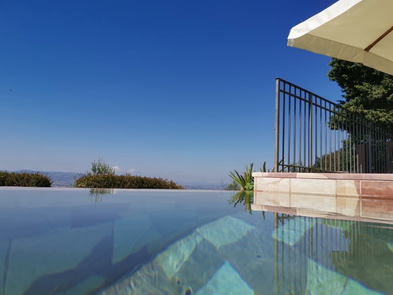 A clear view of an infinity pool with a metal railing and a white umbrella.