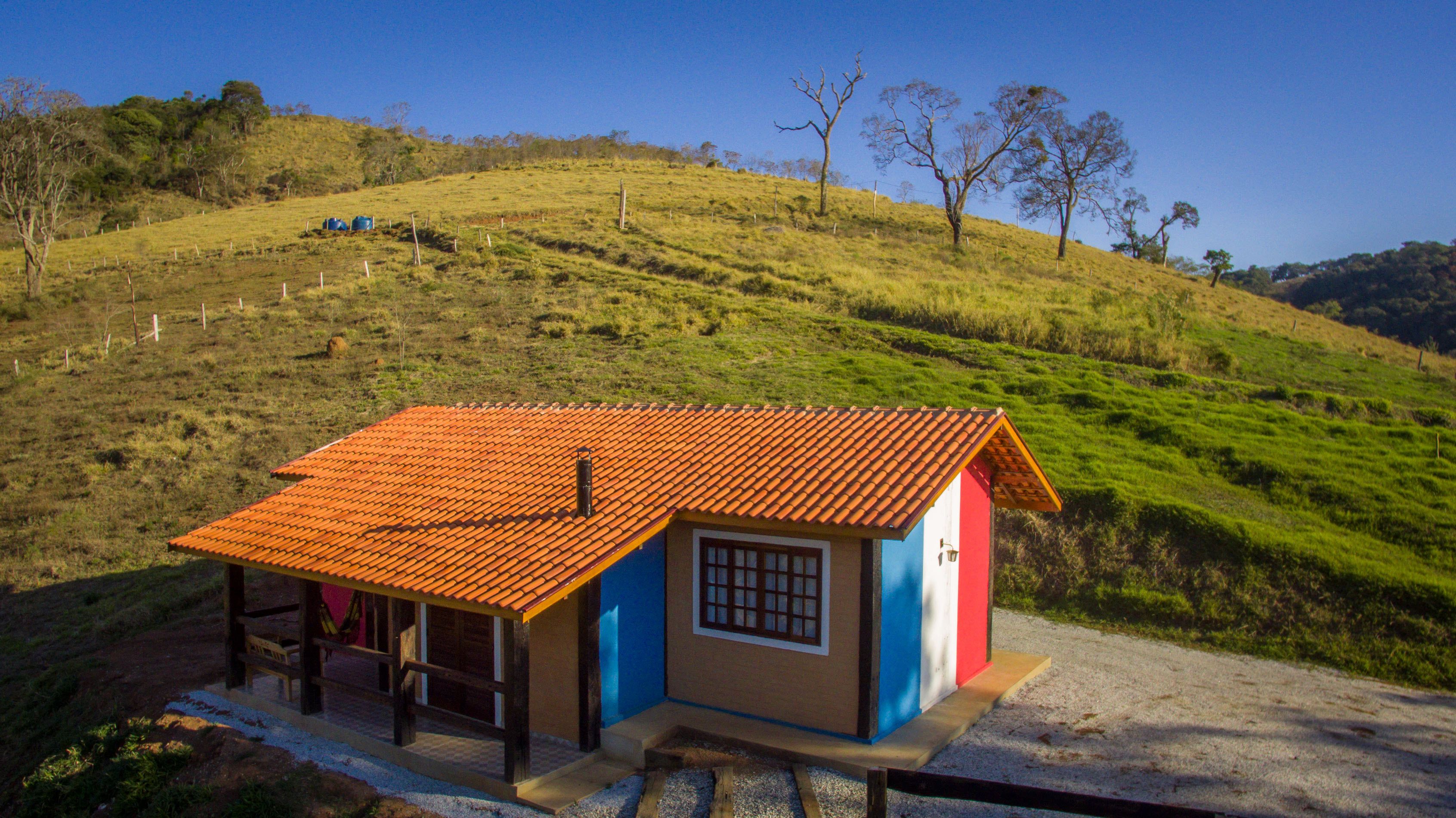 A small house with a red-tiled roof, a blue and red facade, and a wooden porch.