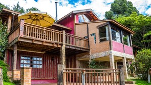 A two-story wooden house with a balcony, a covered porch, and a brick exterior. - Pousada Cabanas no Mundo (Gonçalves)