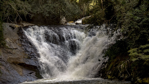 A waterfall cascading over rocks in a forested area. - Pousada Cabanas no Mundo (Gonçalves)