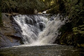 A waterfall cascading over rocks in a forested area. - Pousada Cabanas no Mundo (Gonçalves)