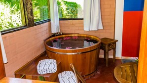 A wooden bathtub with rose petals, a wooden bench, and a small table. - Pousada Cabanas no Mundo (Gonçalves)