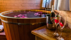 A wooden bathtub filled with water and rose petals, a bottle of champagne, and two glasses with rose petals. - Pousada Cabanas no Mundo (Gonçalves)