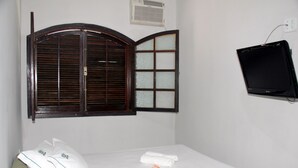 A hotel room with a bed, a window with wooden shutters, a wall-mounted TV, and a small air conditioning unit. - Hotel Chalé São Jorge (Aparecida)