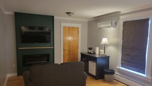 Un salon moderne doté d’un téléviseur à écran plat, d’une chemin ée, d’un canapé, d’un petit bureau avec une lampe et d’une fenêtre avec des stores.