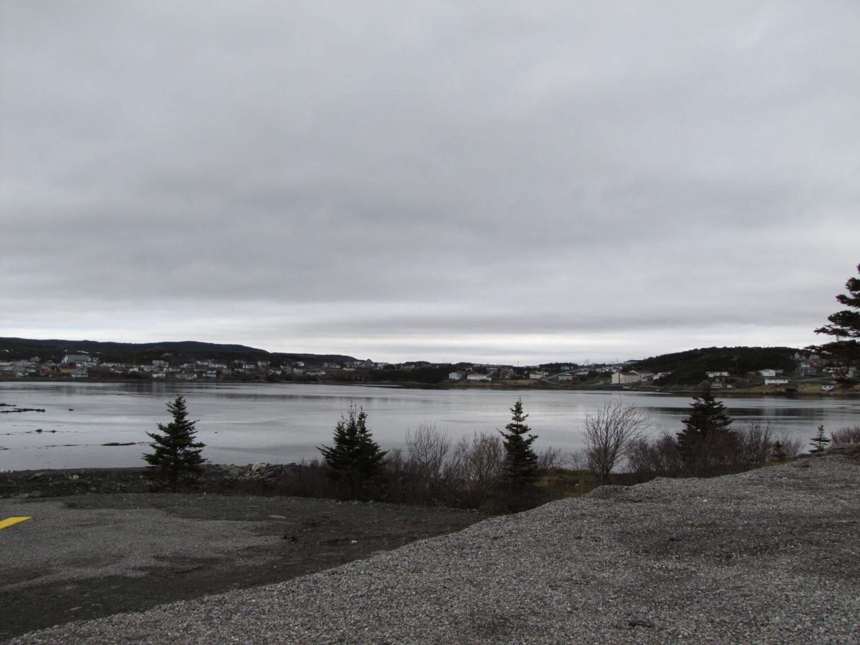 A gravel parking area with a view of a lake and a distant town.
