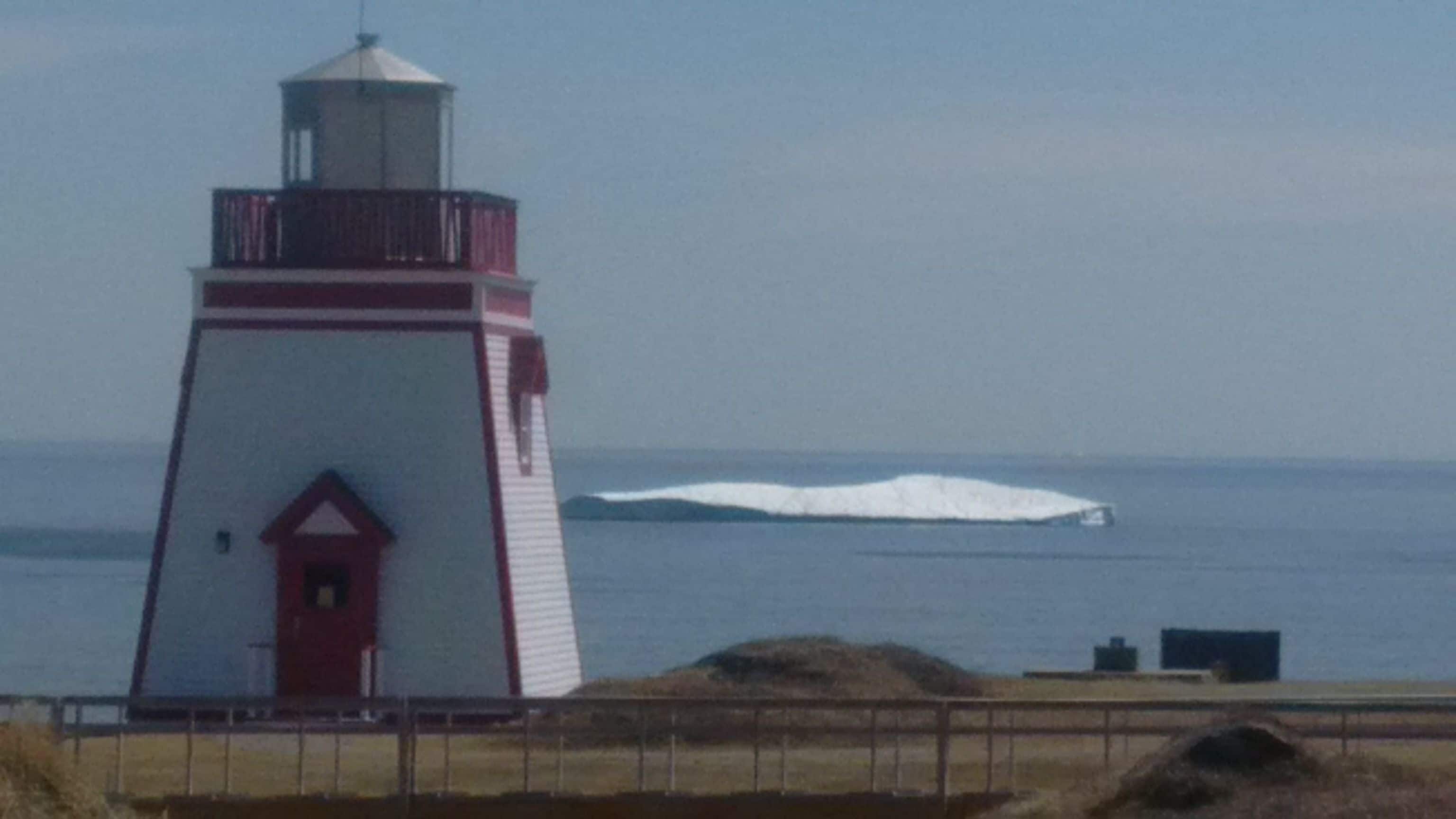 A lighthouse with a red and white structure, located near a body of water with a large wave.
