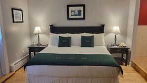 Une chambre d’hôtel bien rangée, avec un grand lit, deux tables de chevet dotées de lampes et des tableaux encadrés accrochés aux murs.