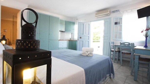 Un dormitorio con cama, una mesita de noche con lámpara, un comedor con mesa y sillas, y una cocina con armarios azules.