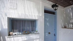 Una puerta blanca con marco azul, una ventana con cortina y un estante con adornos.