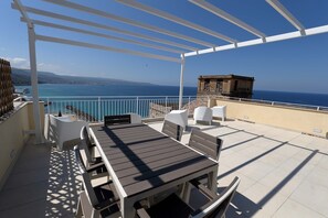 A terrace with a table and chairs, overlooking a coastal view.