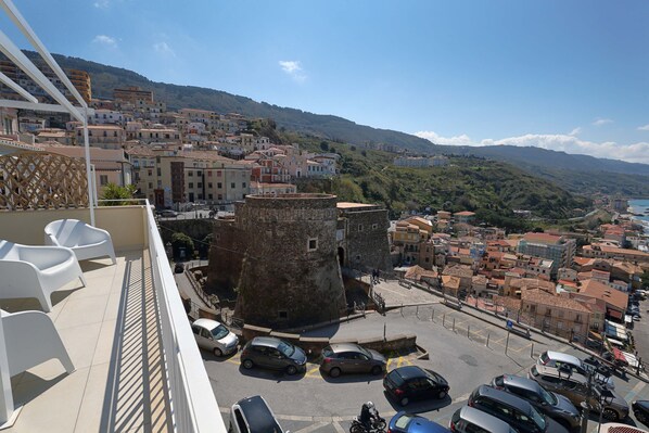A balcony with white plastic chairs, a stone tower, and a view of a coastal town with buildings and a hill in the background. - b & b in the historic center, with a panoramic terrace, 400 meters from the sea (Pizzo)