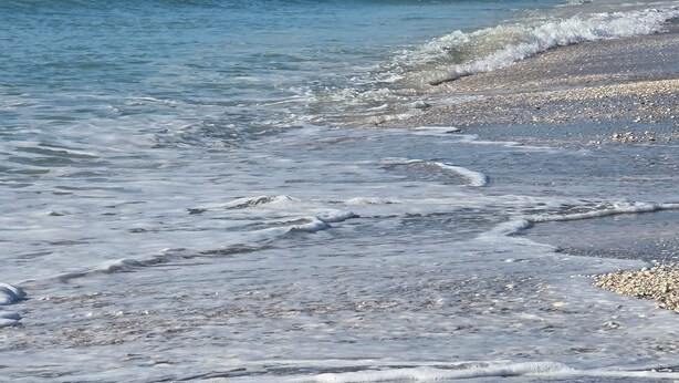 Een strand met helder water, kiezelstenen en een zandstrand.