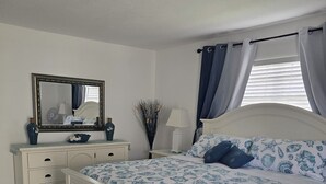 Een slaapkamer met een wit bed, een dressoir, een spiegel en een raam met gordijnen.