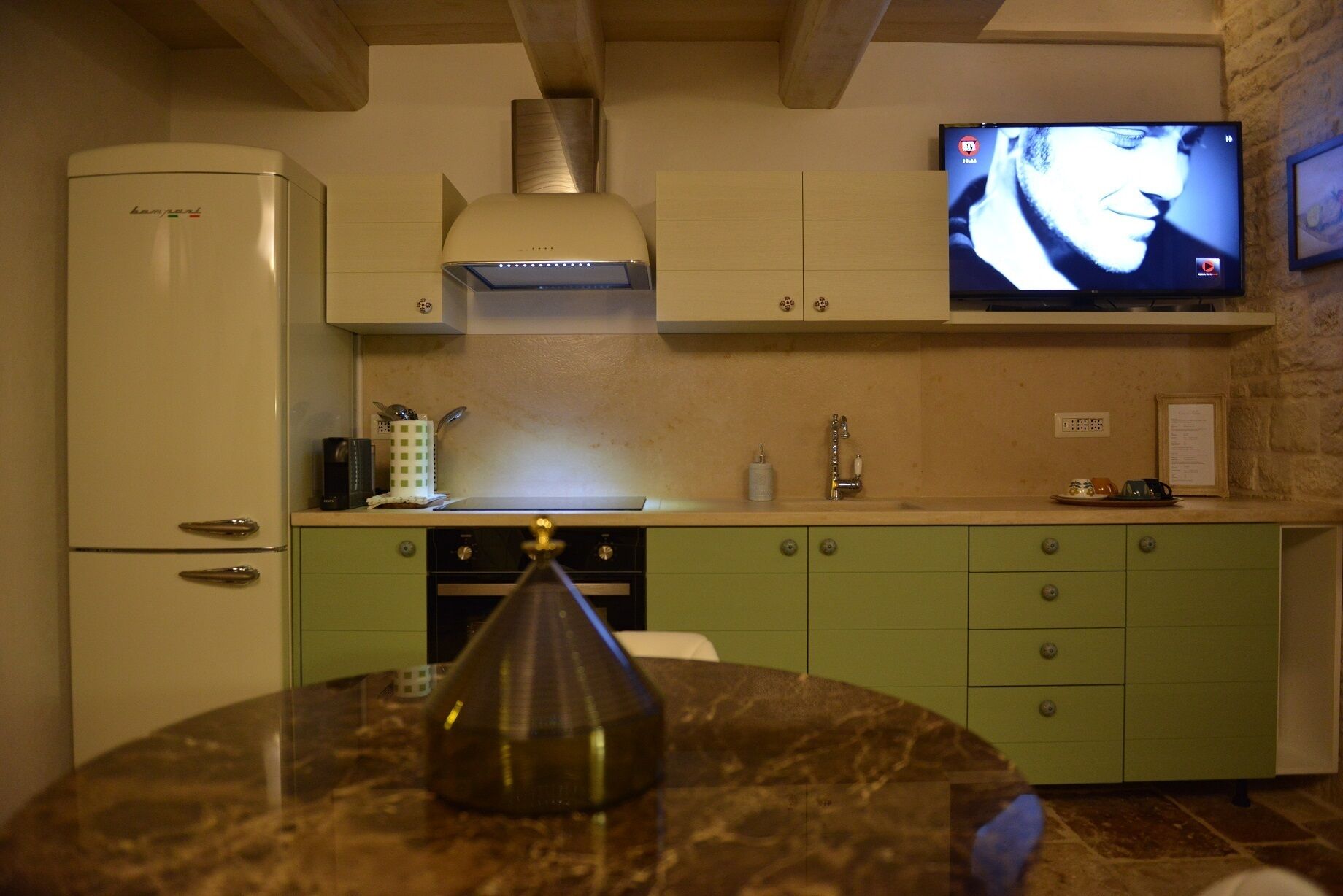 A kitchen with a white refrigerator, a stove, and a television mounted on the wall.