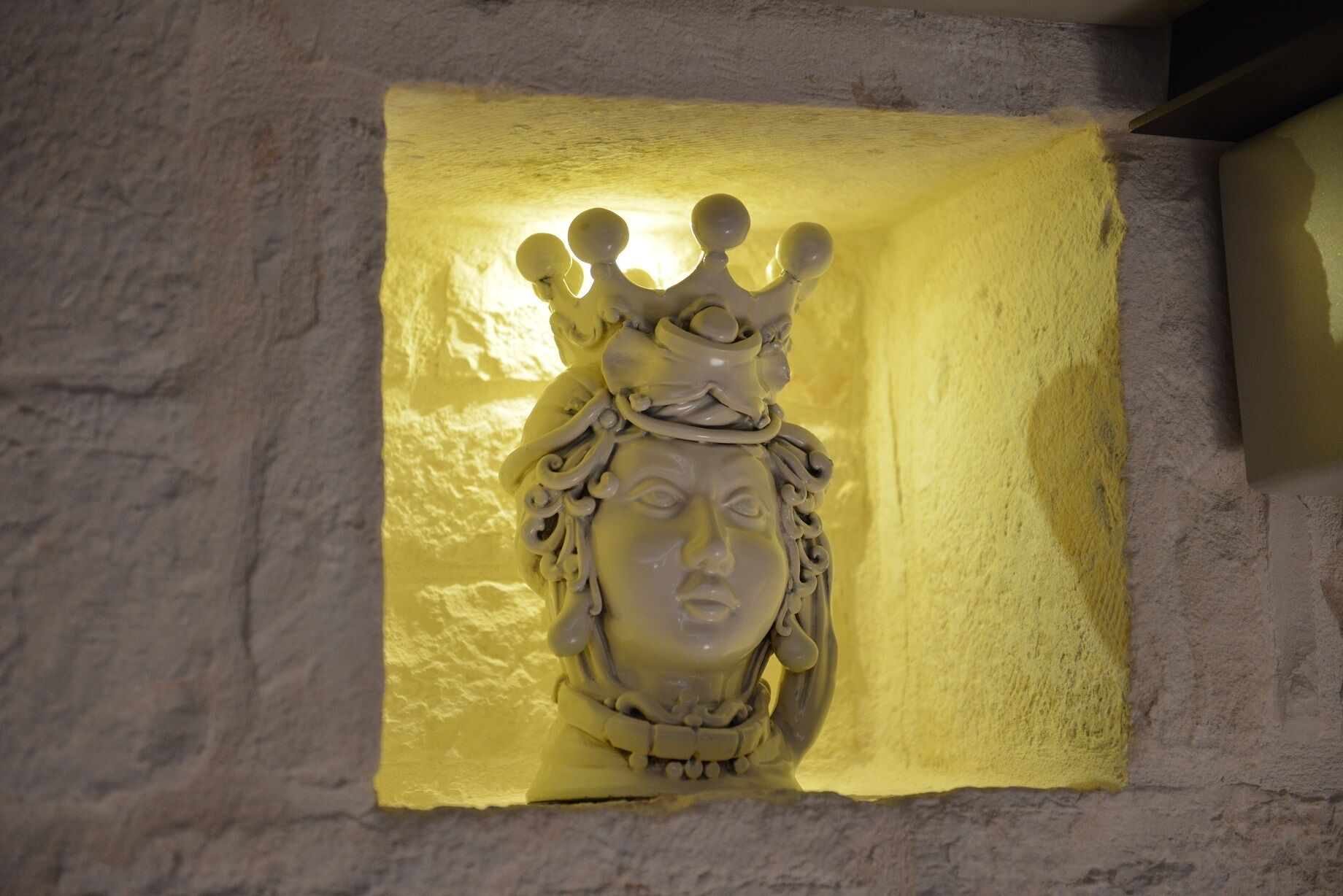 A sculpture of a figure with a crown, set against a textured wall.