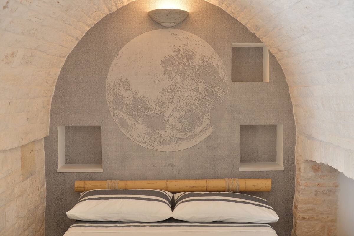 Una habitación con una cama, una pared con un diseño circular y una ventana.