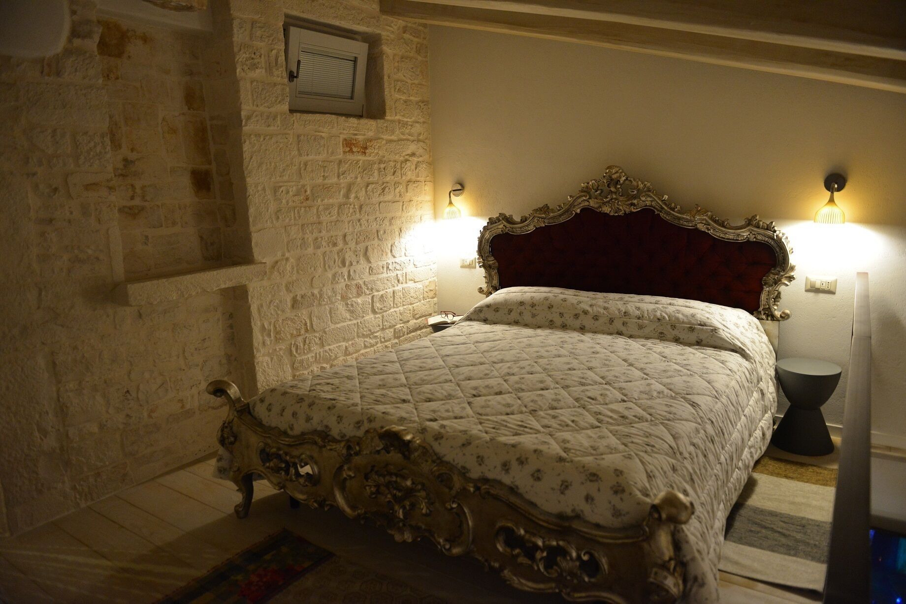 A bedroom with a large bed, ornate headboard, and two wall-mounted lamps.