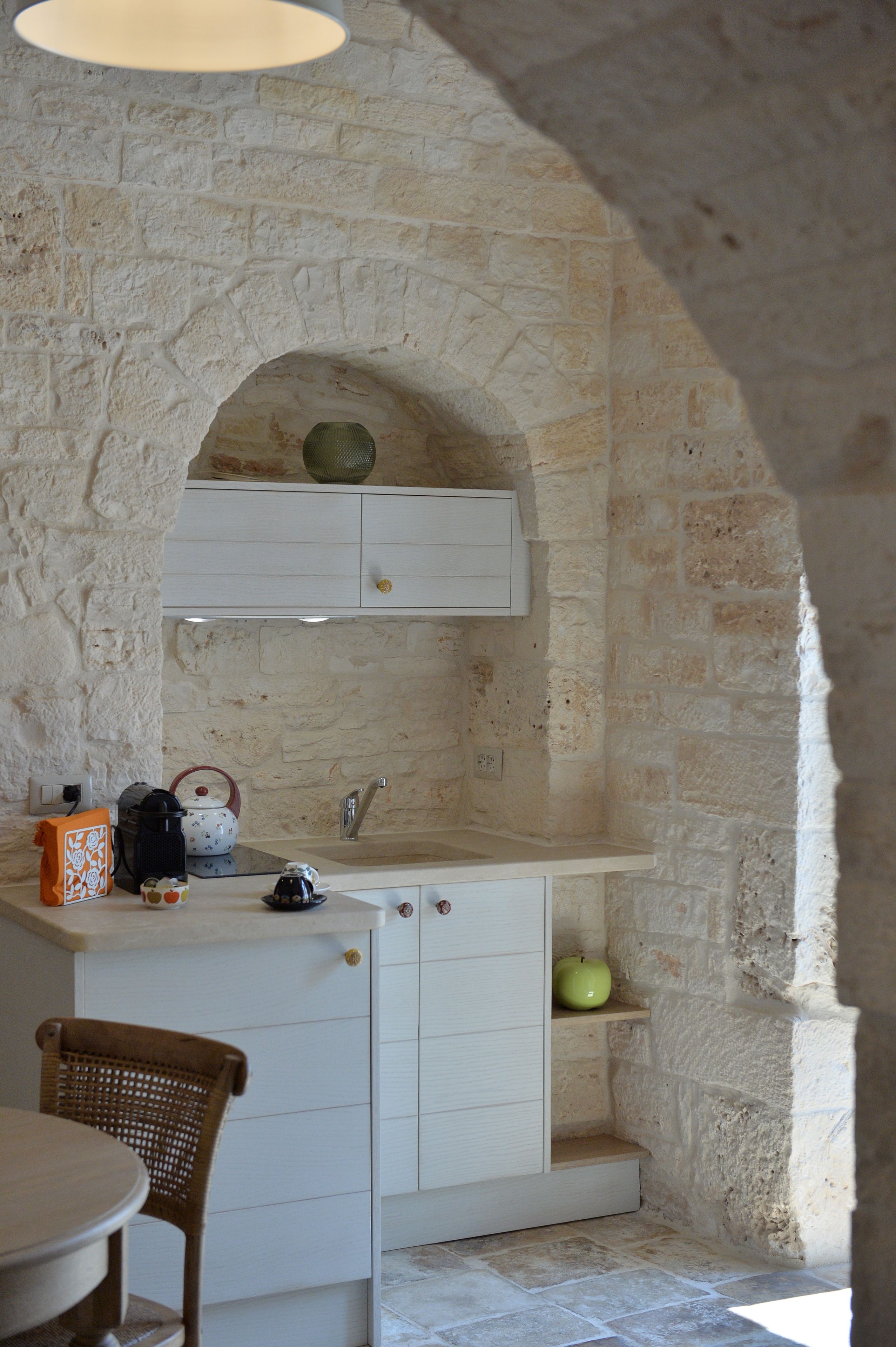 A stone-walled kitchen with a built-in sink, a small shelf, and a chair.