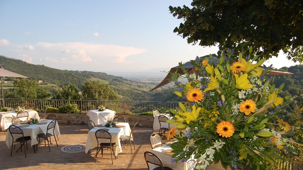 Un espace de restauration en plein air, avec des tables et des chaises, entouré d’un paysage pittoresque composé de collines et d’un ciel dégagé.